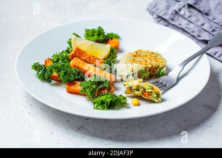 Concept de cuisine végétarienne. Côtelette de légumes avec patate douce cuite au four et kale sur une assiette blanche. Banque D'Images