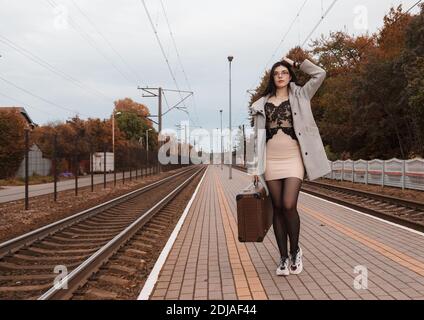 petite fille solitaire en manteau gris avec une valise debout à gare le jour sombre de l'automne Banque D'Images