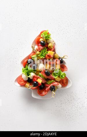 Canapés de Noël dans une assiette en forme d'arbre de Noël pour les fêtes de Noël sur table blanche. Vue de dessus. Format vertical. Banque D'Images