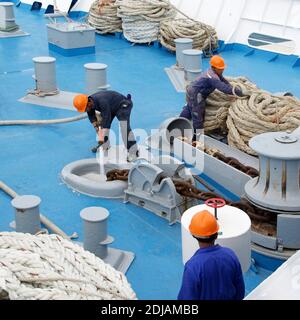 Marins et marins de la marine marchande travaillant ensemble avant la croisière équipage de pont de navire empilant l'étaleur de corde d'amarrage et chaîne d'ancrage de flexible de pression Banque D'Images