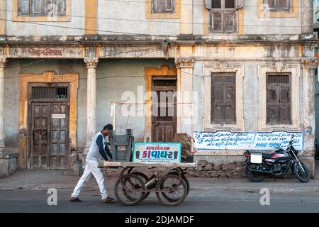 Jamnagar, Gujarat, Inde - décembre 2018 : un vendeur indien de nourriture de rue pousse sa charrette devant un vieux bâtiment d'époque dans la ville de Jamnagar. Banque D'Images