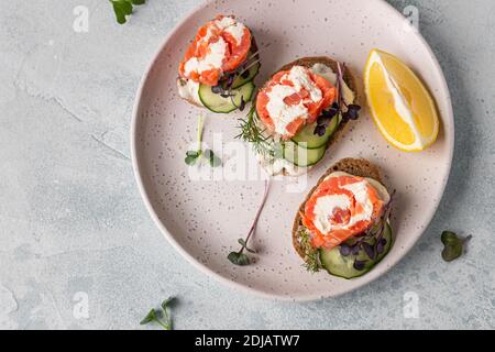 Mini-sandwiches ouverts avec saumon fumé, fromage à la crème, concombre et micro-vert sur pain de seigle, fond de pierre grise. Apéritif avec saumon et fromage c Banque D'Images