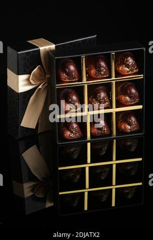 Des bonbons faits main de luxe peints dans une boîte cadeau sur fond noir. Chocolats pour la Saint-Valentin. Banque D'Images