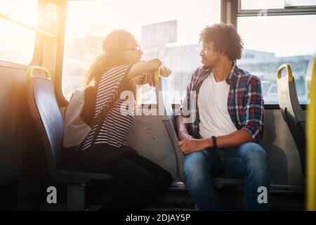 Jeune belle fille est assise dans un bus se penchant contre le siège du jeune homme beau qui est tourné vers elle pendant qu'ils voyagent en bus et chat Banque D'Images