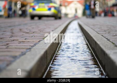 Gros plan sur un chenil rempli d'eau sur le pavé de la rue de Fribourg, en Allemagne. La voiture de police et les piétons sont flous en arrière-plan. Niveau du sol s Banque D'Images