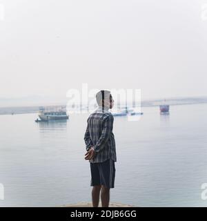 Un homme debout sur les ghats de la rivière ganga dans la ville sainte de varanasi, Sutter pradesh inde. Il porte un masque, mais pas de manière appropriée Banque D'Images