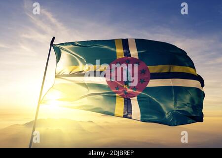 Drapeau de la Dominique agitant sur le brouillard de lever de soleil supérieur Banque D'Images