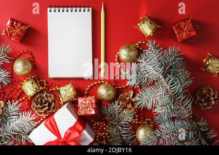 Bloc-notes et crayon pour écrire des voeux et des cadeaux pour le nouvel an et Noël autour des décorations d'arbre de Noël sur un fond rouge. Nouvel an moo Banque D'Images