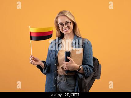 Bonne jeune femme blonde étudiante dans une ambiance décontractée avec des lunettes, un sac à dos et des livres tenant un petit drapeau de l'Allemagne Banque D'Images