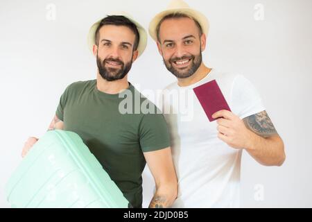 Jeune gay couple de deux hommes tenant une valise en vacances d'été sur fond blanc. Banque D'Images