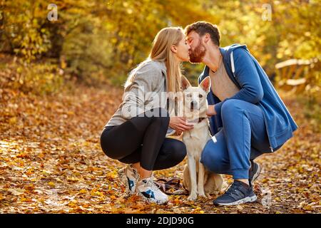 portrait de couple charmant dans la forêt, homme caucasien et femme embrassant, tenant chien blanc dans les mains Banque D'Images