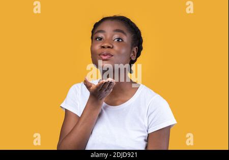 Jolie femme noire soufflant UN Kiss posant sur fond jaune Banque D'Images