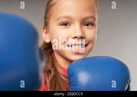 Gros plan d'un adorable boxeur féminin pour enfants regardant l'appareil photo et souriant tout en faisant la posture de combat Banque D'Images