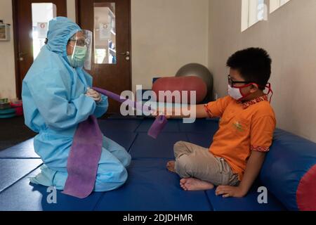 BALI/INDONÉSIE-OCT 23 2020: Un enfant ayant un handicap physique est en train de faire une thérapie physique. Ils portent des masques et une combinaison de hamzat pour éviter la propagation du C Banque D'Images