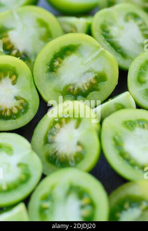 Solanum lycopersicum. Tomates vertes non mûres coupées en deux sur une plaque d'ardoise. ROYAUME-UNI Banque D'Images