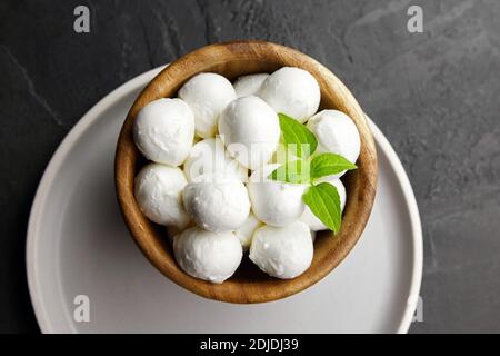 Mini boules de fromage mozzarella dans une assiette en bois sur fond de caillou noir, vue du dessus. Produits laitiers italiens traditionnels. Banque D'Images