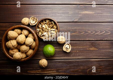 Noix dans un bol rond sur une table en bois. Noyer non mûr avec péricarpe verte et graines sèches sur fond marron, nourriture saine, vue du dessus Banque D'Images