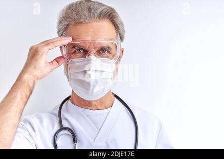 un médecin de race blanche, un homme en lunettes de protection, le portant avant de travailler avec des patients, regarde la caméra Banque D'Images