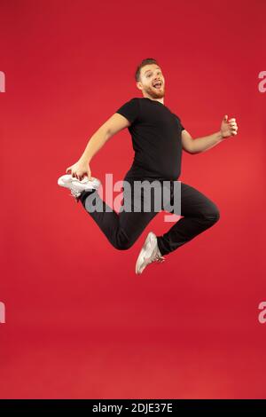 Inspiré. Portrait complet de jeune homme de saut haut réussi gesturant isolé sur fond rouge studio. Modèle caucasien mâle attrayant. CopySpace. Émotions humaines, concept d'expression faciale. Banque D'Images