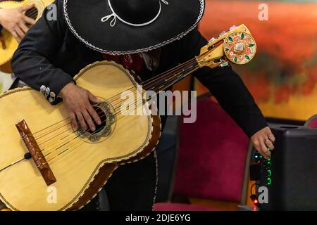 Concentration sélective des mains du jeune homme mariachi, tenant et jouant de la guitare basse acoustique avec orchestre et régler le volume pendant le festival de dia de los muertos Banque D'Images