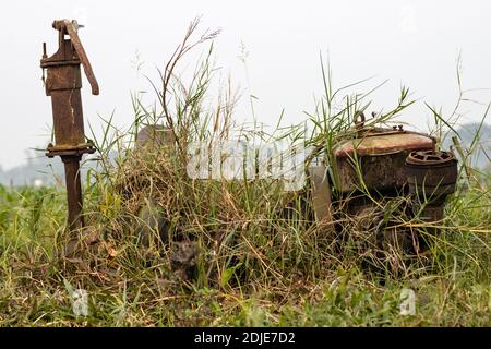 Une vieille pompe à eau rouillée inutile à l'intérieur de l'herbe la terre agricole dans le village rural Banque D'Images