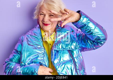 une dame âgée sympa qui se pose isolée en studio sur fond violet, une femme mûre regarde la caméra et sourit, se rendant à la fête Banque D'Images