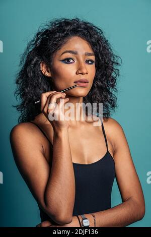 Photo de la jeune femme hispanique portant un maquillage frais à l'aide d'un rouge à lèvres et regardant l'appareil photo. Banque D'Images