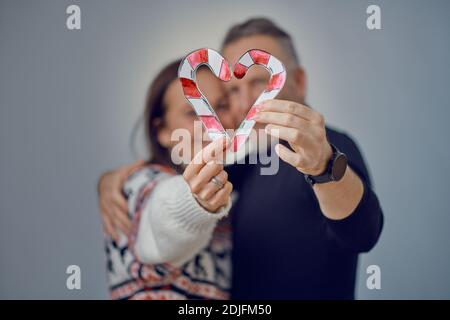 Incognito adulte couple dans le concept d'amour de Noël, tenant des cannes en papier coupé dans une forme de coeur dans leurs mains, se tenant près et embrassant. BL Banque D'Images