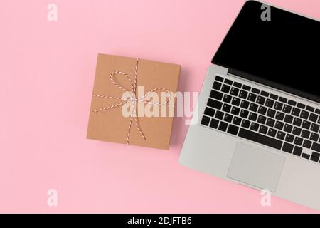 Plat avec ordinateur portable et boîte cadeau sur fond rose. Composition minimaliste des achats en ligne. Banque D'Images
