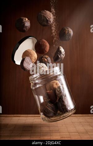 composition photographique créative de délicieux truffes au chocolat volant et flottant pot en verre sur fond en bois Banque D'Images