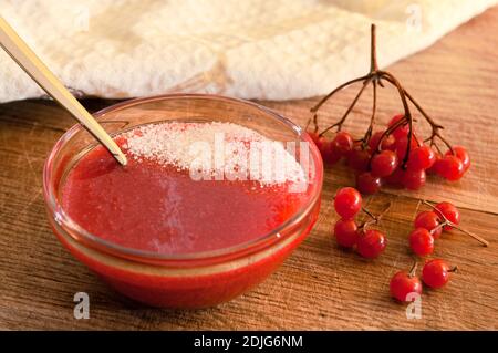 Baies rouges d'un viburnum moulu avec du sucre dans un vase en verre sur une table en bois. La douceur de la vitamine. Banque D'Images