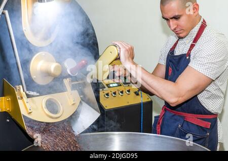 Les mains de l'homme torréfaction des grains de café aromatiques sur un moderne machine utilisée pour rôtir les grains Banque D'Images