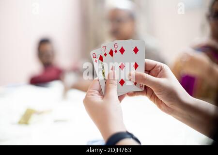 Femme tenant des cartes avec des membres de famille hors foyer dans la distance montrant une famille jouant des cartes dans des festivals comme diwali, dusera, nouvel an et Banque D'Images