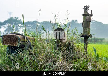 Pompe à eau rouillée inutile dans le champ agricole à l'intérieur du herbes sauvages Banque D'Images