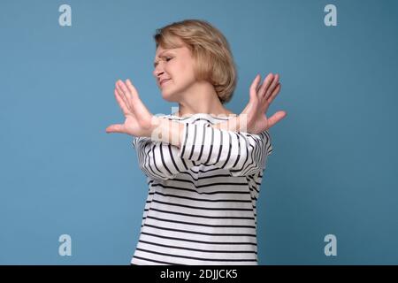 Femme âgée debout avec les mains croisées et montrant un geste d'arrêt sur fond bleu Banque D'Images