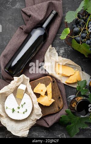 Bouteille de vin rouge fromage Camembert et fromage vieilli, raisins. En-cas au bar à vins. Composition de vin sur fond de béton rustique foncé. Récolte verticale à plat Banque D'Images