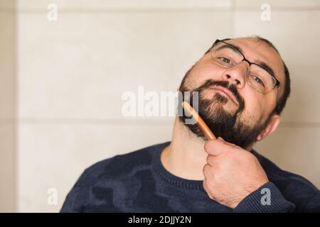 Homme en lunettes peignez sa barbe à l'intérieur Banque D'Images