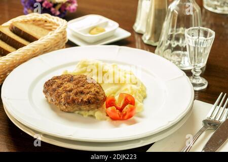 Assiette blanche, servie sur une table en bois brun avec des côtelettes frites, une purée de pommes de terre et des tomates fraîches rouges. Concept de nourriture saine et savoureuse. Banque D'Images