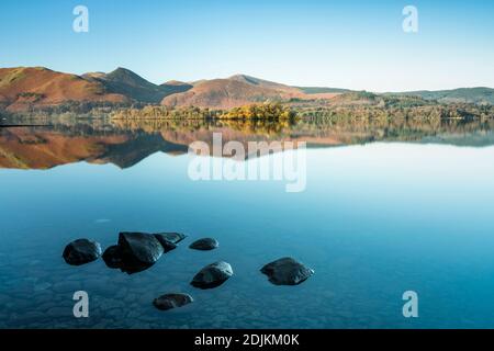 Roches de premier plan montrant à travers un Derwentwater très calme, avec les fells du nord-ouest reflétés dans le fond. Lake District, Cumbria, Angleterre Banque D'Images