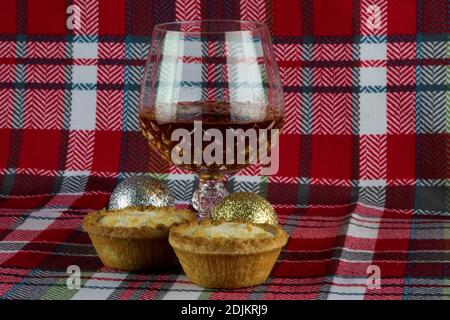 Tartes de Noël au mini-plat et verre de brandy avec boules de Noël sur un chiffon de table tartan Banque D'Images