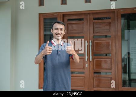 un homme asiatique se tient debout avec les pouces contre le nouveau fond de la maison Banque D'Images