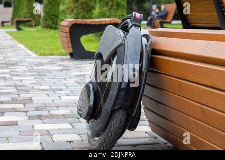 Monoroue électrique noire, véhicule personnel innovant, monocycle électrique auto-équilibré, transport urbain écologique du futur près d'un banc en bois Banque D'Images