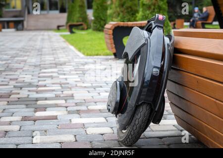 Monoroue électrique noire, véhicule personnel innovant, monocycle électrique auto-équilibré, transport urbain écologique du futur près d'un banc en bois Banque D'Images