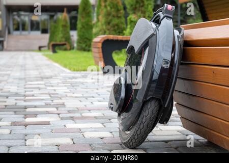 Monoroue électrique noire, véhicule personnel innovant, monocycle électrique auto-équilibré, transport urbain écologique du futur près d'un banc en bois Banque D'Images