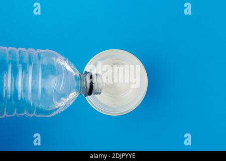 poser à plat avec de l'eau qui coule de la bouteille en plastique au verre sur fond bleu. Banque D'Images