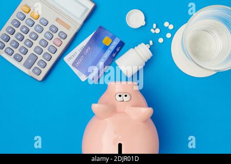 flat lay avec des pilules, banque de porc, verre d'eau, cartes de crédit et calculatrice sur fond bleu. Banque D'Images