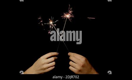 Gros plan des mains ou des paumes tenant et agitant les spameurs brûlants devant un arrière-plan noir foncé. Des lumières étincelantes pour les fêtes d'anniversaire, les mariages, le nouvel an, la veille de Noël, Noël. 6k de mise à niveau vers le bas. Feu Bengale Banque D'Images