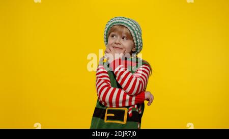 Concept de Noël. Petit amusant blond enfant adolescent adolescente fille 5-6 ans dans Noël elf Santa aide costume espoirs pour les rêves viennent, faire un souhait, prie pour une vie meilleure. Enfant souriant Banque D'Images