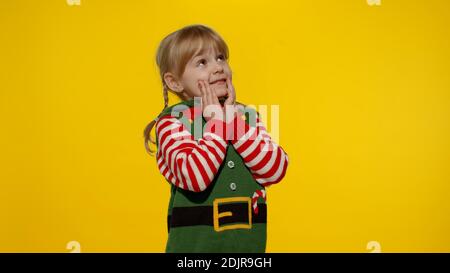 Sly kid teen girl steepls fingers and schemes something gets interesting idea how to decorate house, waiting for gift box. New Year and Christmas holidays winter time. Child Christmas elf Santa helper Stock Photo