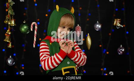 Sly kid teen girl steepls fingers and schemes something gets interesting idea how to decorate house, waiting for gift box. New Year and Christmas holidays winter time. Child Christmas elf Santa helper Stock Photo